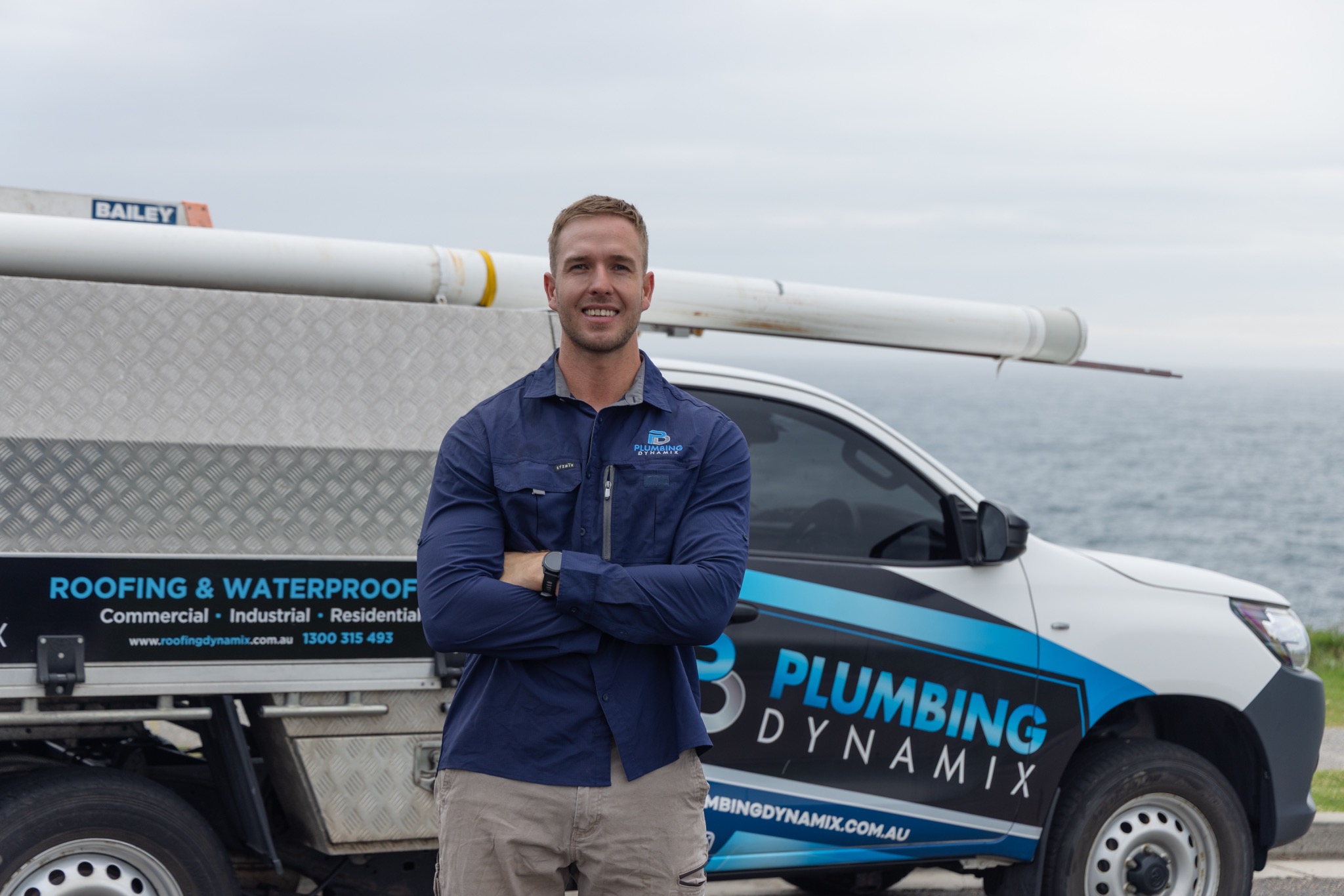 Plumbing Dynamix plumber beside a branded service vehicle